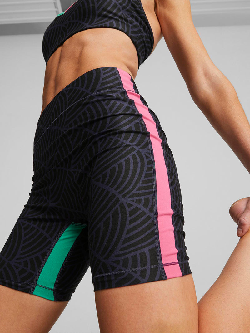 Close up on a Woman Exercising wearing Puma x lemlem low impact bra in navy and black colors and Puma x lemlem bike shorts in navy and black colors featuring hand sketched scallop print and color block accents in bright pink and turquoise colors