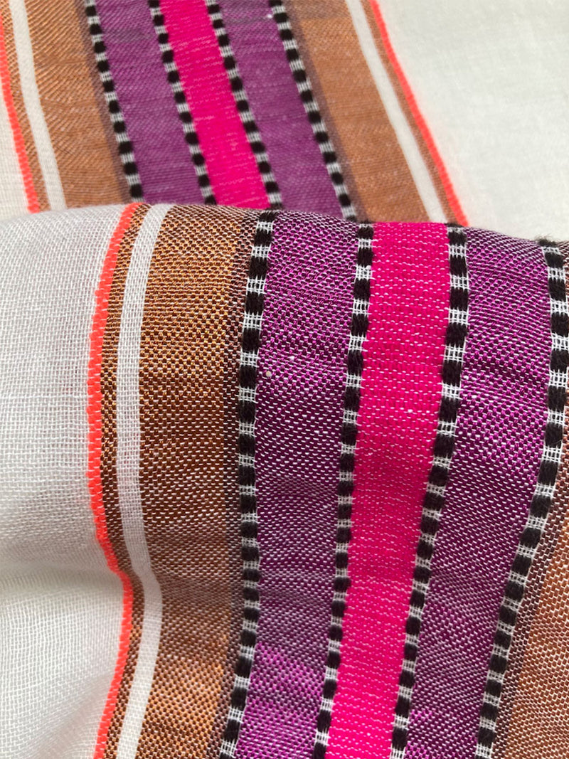 Close up on the fabric of the Lema Sarong featuring stripe pattern in magenta, ochre, and berry tones, delineated by black and white dots and accented with a splash of neon orange on natural cotton background