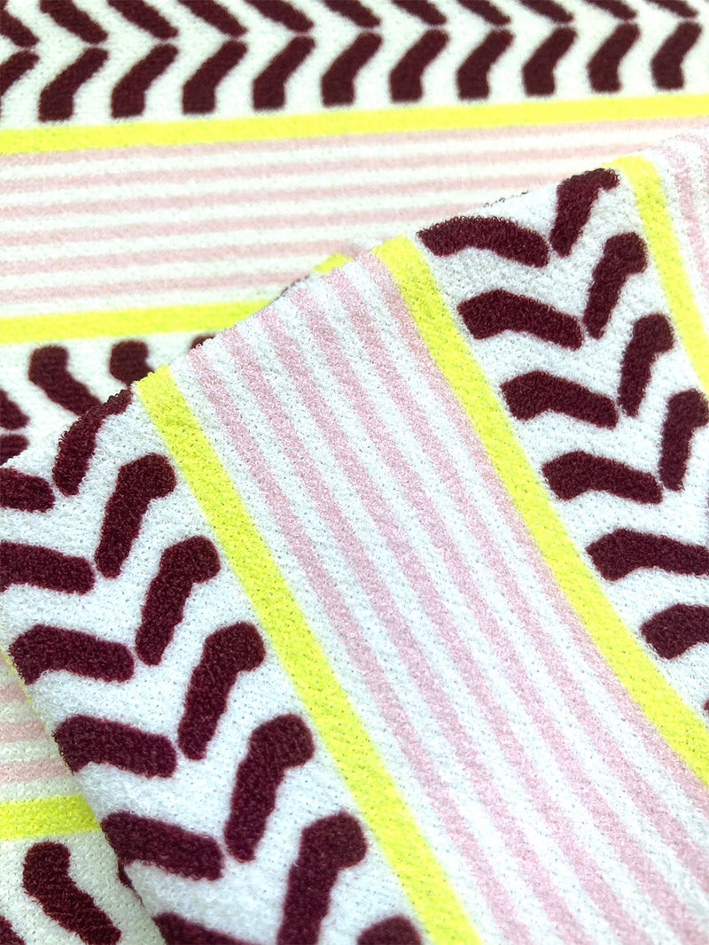 Close up on the fabric of the Rekka String Bottom featuring a range of subtle hues from pink to burgundy with an accent of citron. It features a bold chevron pattern over a delicate pink striped micro terry texture. Contrasting ivory fabric is printed with pink stripes and geometric shapes.