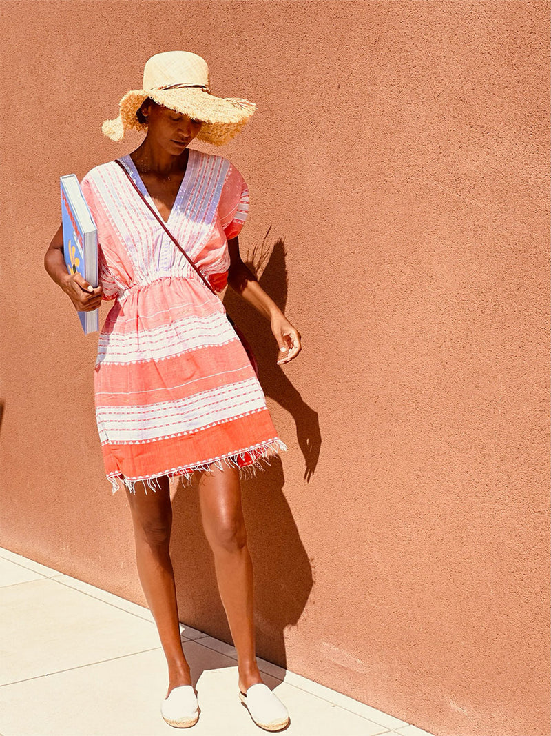 Liya Kebede standing holding a book in her hand wearing Eshal Short Plunge Neck Dress and a straw hat