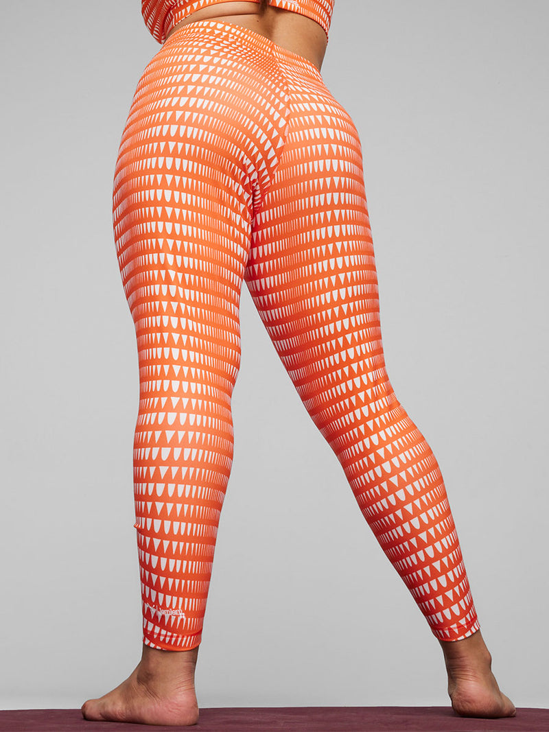 Back View of a Woman Standing Wearing Puma x lemlem Leggings in Cayenne Pepper Color featuring lemlem triangle pattern in white color