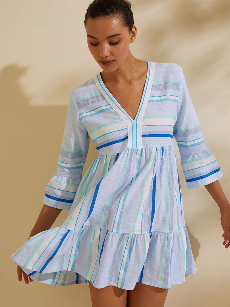 Woman standing wearing the Ruki Flutter Dress featuring a mutli tonal stripe pattern in five shades of blue with silver and white accents.