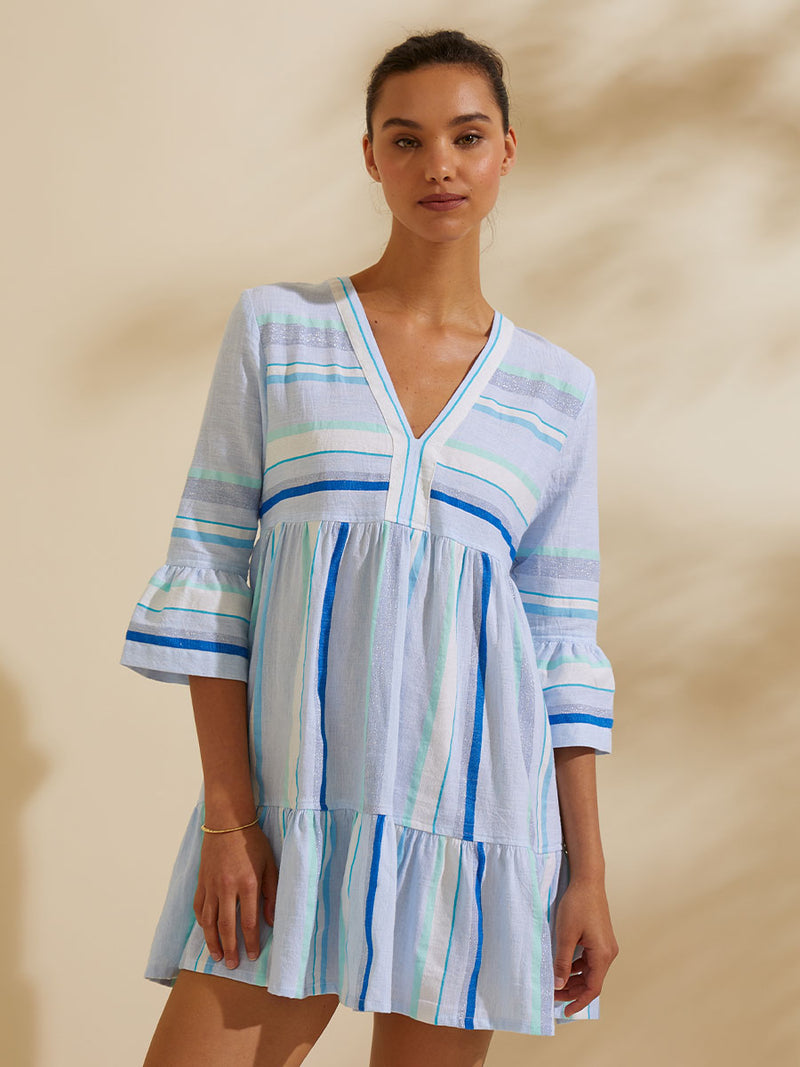 Woman standing  wearing the Ruki Flutter Dress featuring a mutli tonal stripe pattern in five shades of blue with silver and white accents.