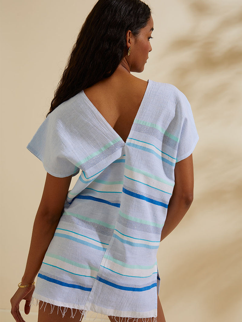 Back view of a woman standing wearing the Ruki Split Tunic featuring a mutli tonal stripe pattern in five shades of blue with silver and white accents.