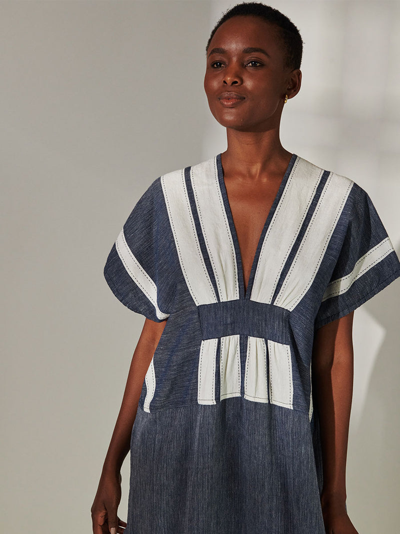 Close up on a Woman Standing Wearing lemlem Gasira V Neck Caftan Featuring Bold Stripe Pattern with pick stitch edge in Classic Navy and White colors.
