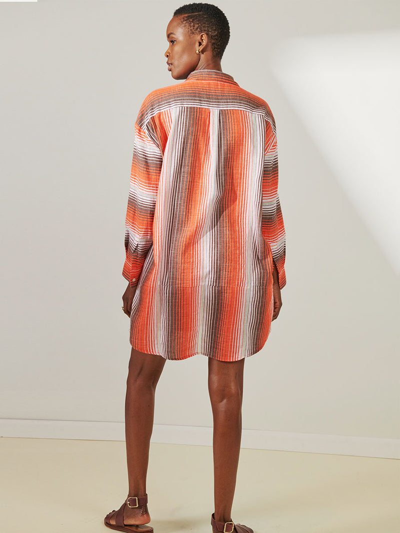 Back View of a Woman Standing Wearing lemlem Mariam Shirt featuring graded continuous stripe pattern creating an ombre effect featuring earth, orchid & burnt orange