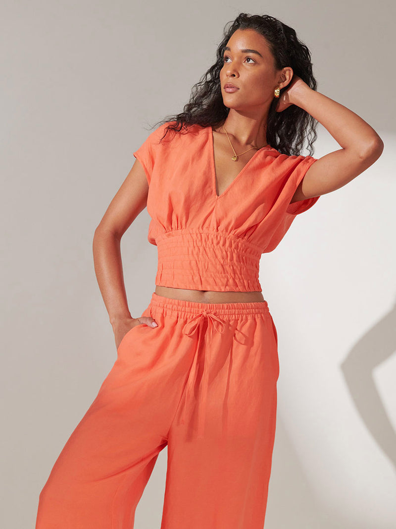 Woman standing wearing lemlem Alia Plunge Top in Coral Color and Desta Pants in Coral Color