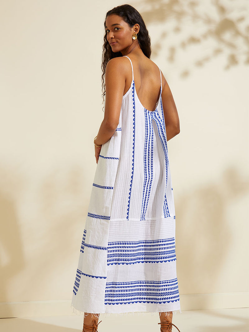 Back view of a woman standing wearing the Yani Slip Dress featuring blue tibeb diamond design bands on a textured seersucker white background.  