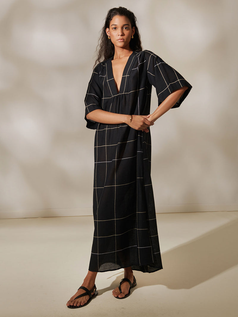 Woman Standing Wearing Edna V Neck Maxi Dress featuring Big White Plaid Patten on Black Cotton Background