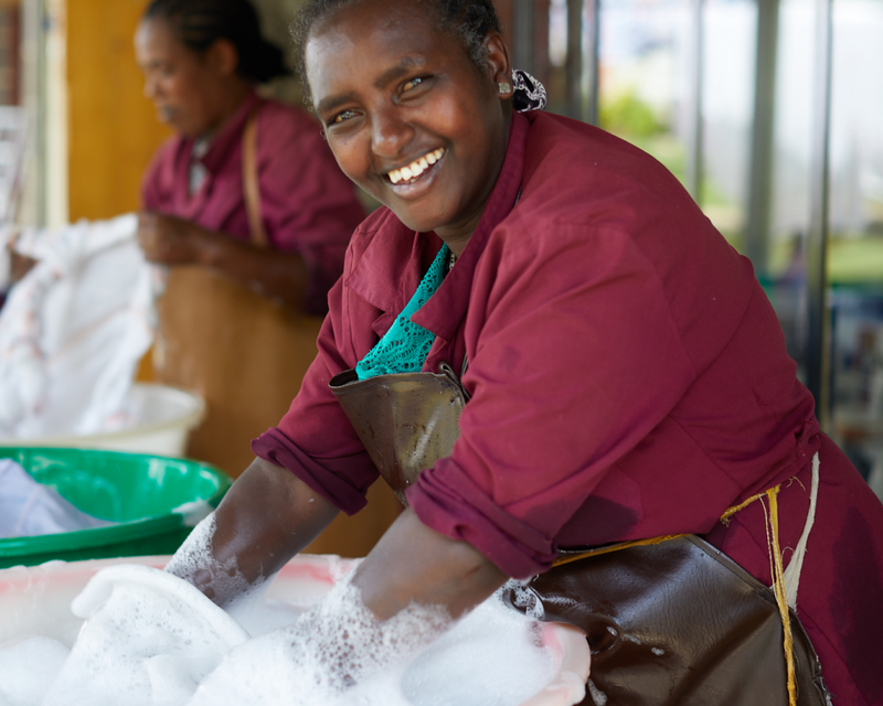 A smiling woman artisan washing the cotton fabric by hand in Ethiopia outside