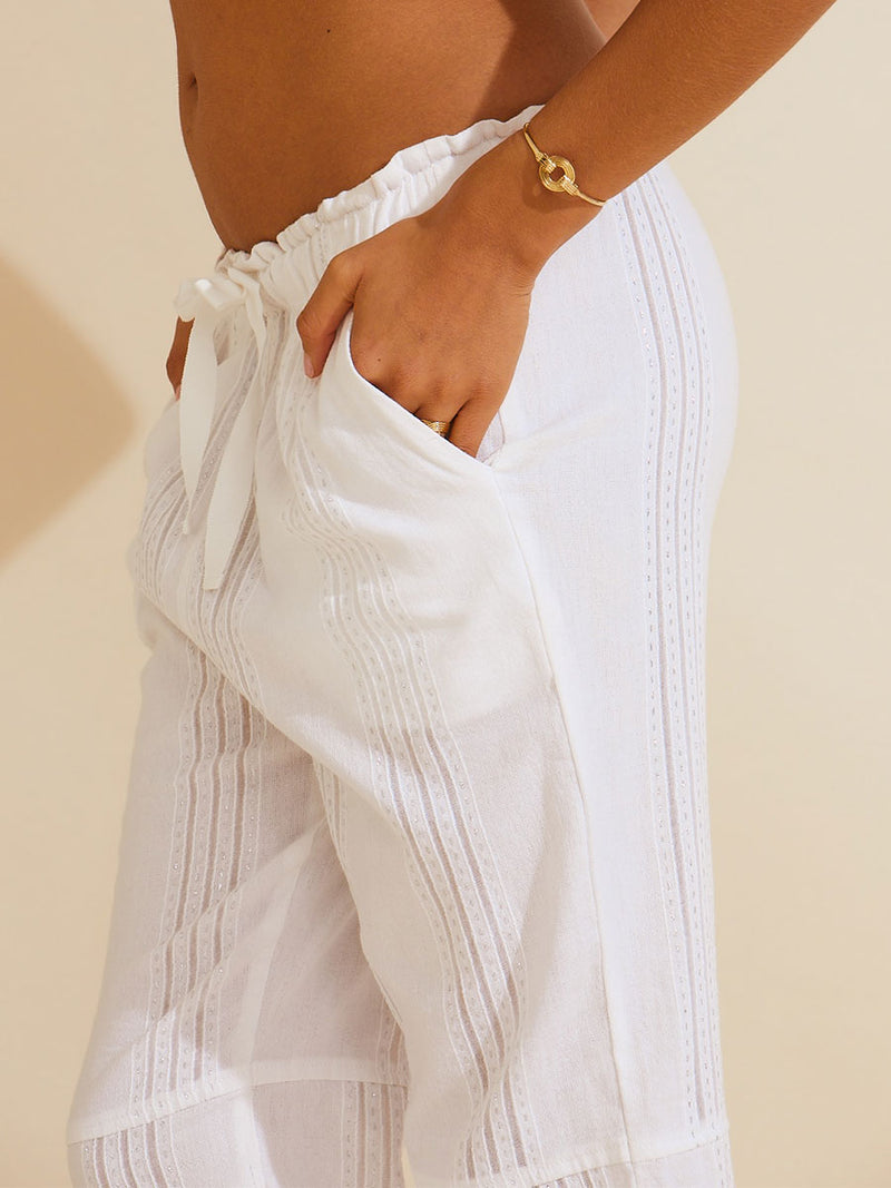 Close view of a woman standing with her hand in her pocket wearing the Abira Drawsting Pants in white with silver lurex.