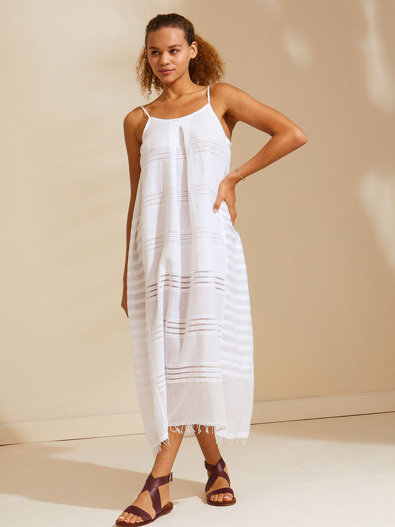 Woman standing with her hand on her hips wearing a white Abira long slip dress with spaghetti straps and stitches of silver lurex