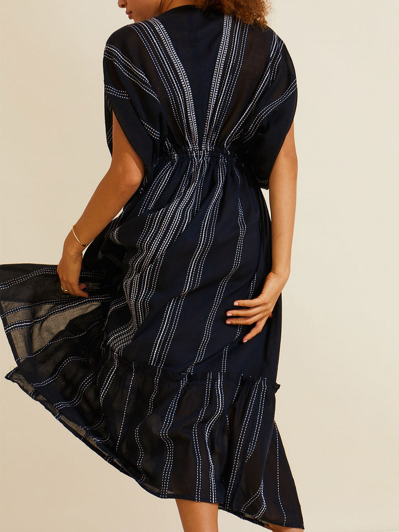 Back view of a woman standing wearing the Leliti Plunge Neck Dress in Black with white stitching allover.