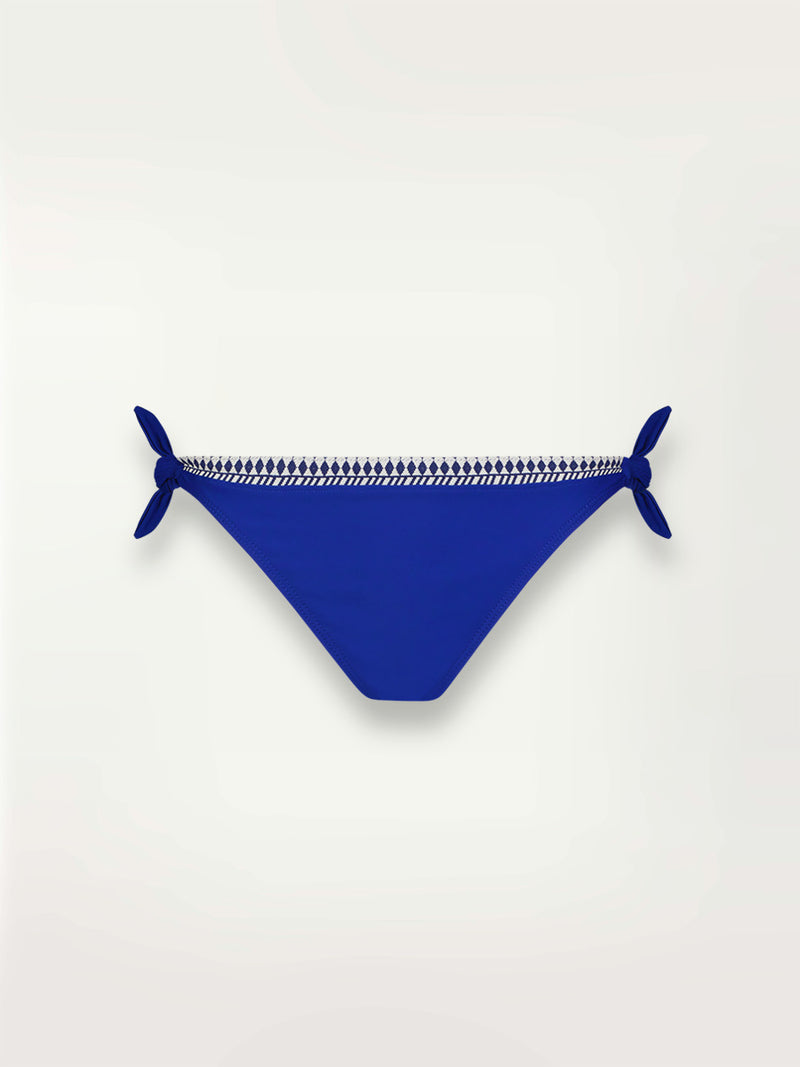 Product shot of the Lena Side Tie Bikini Bottom  in bright neon blue adorned with navy and white diamond jacquard pattern on the trims