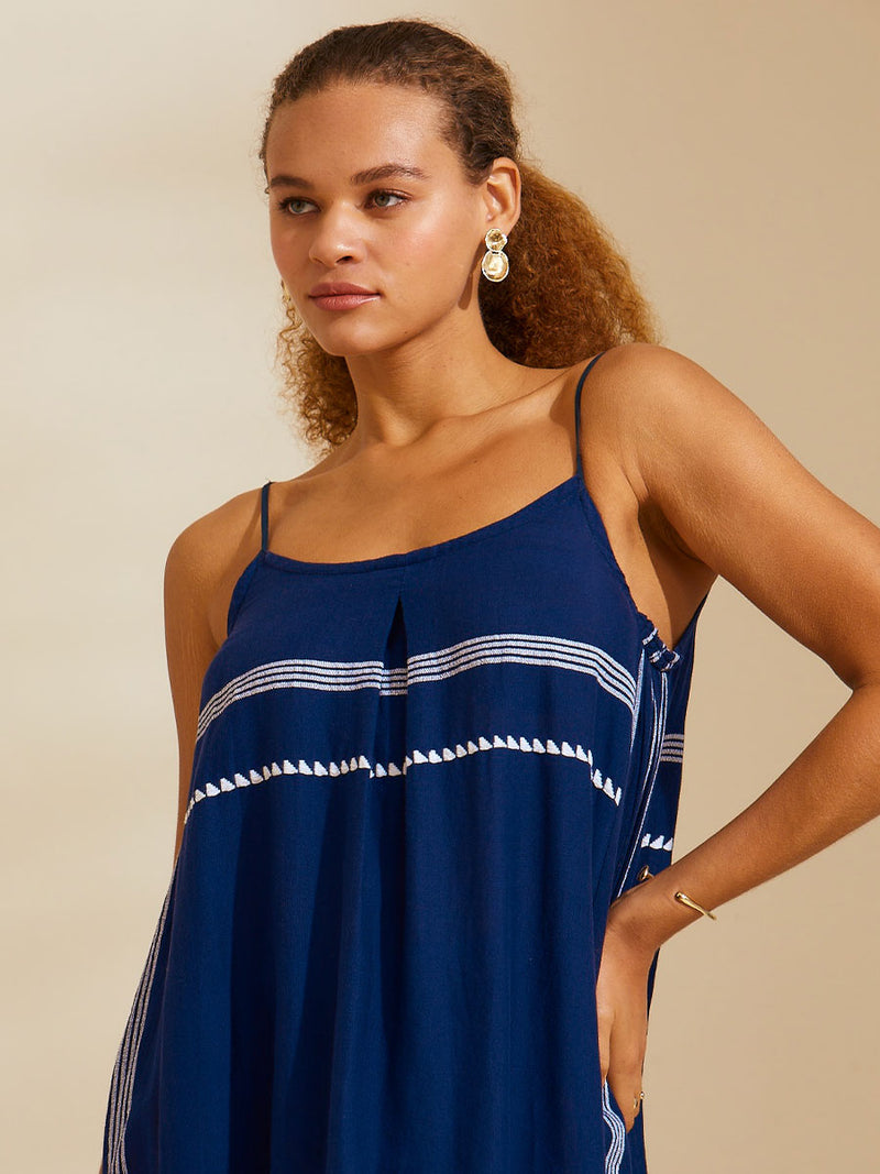 Close up view of a woman standing with her hand on her hip wearing the Nunu Long Slip Dress in navy blue featuring white stripes and graphic lines.