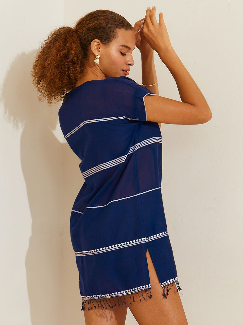 Side view of a woman standing her hands up by her face wearing the Nunu Tunic Dress in navy blue featuring white stripes and graphic lines