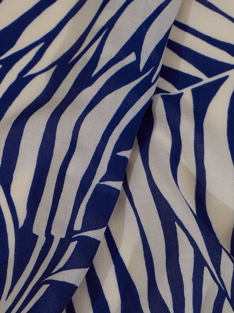 Close up on the fabric of the Palm Leaf Flutter Sleve Mini Dress featuring palm tree patterns on a rich blue background.