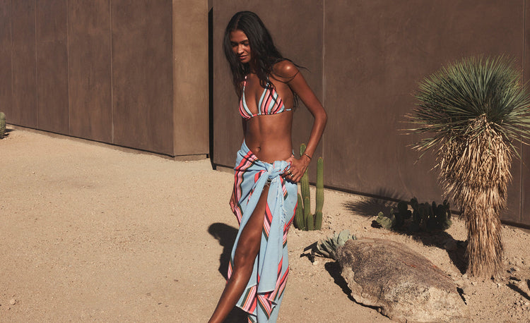 Woman standing wearing lemlem handwoven shirt and shorts featuring navy stitching on white background