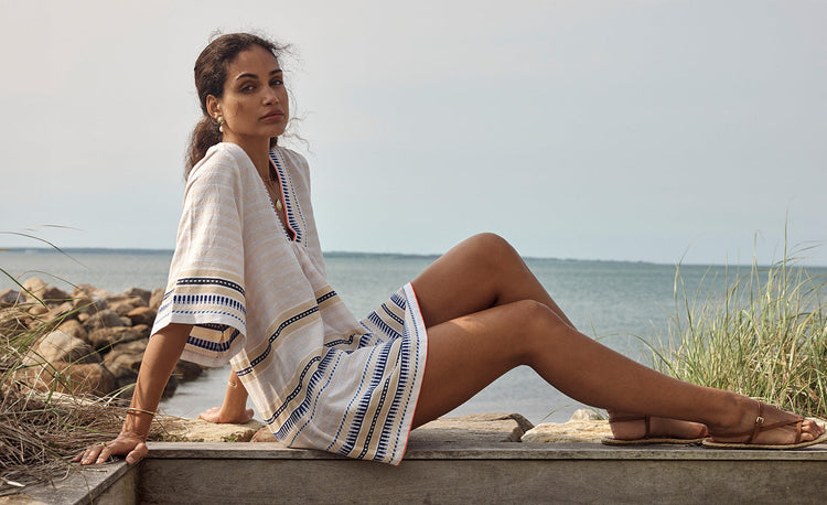 Woman Sitting wearing lemlem handwoven caftan featuring tibeb pattern in navy color on cream background