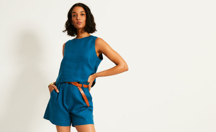 Woman standing with her hands in her pockets wearing linen lemlem pants in teal blue