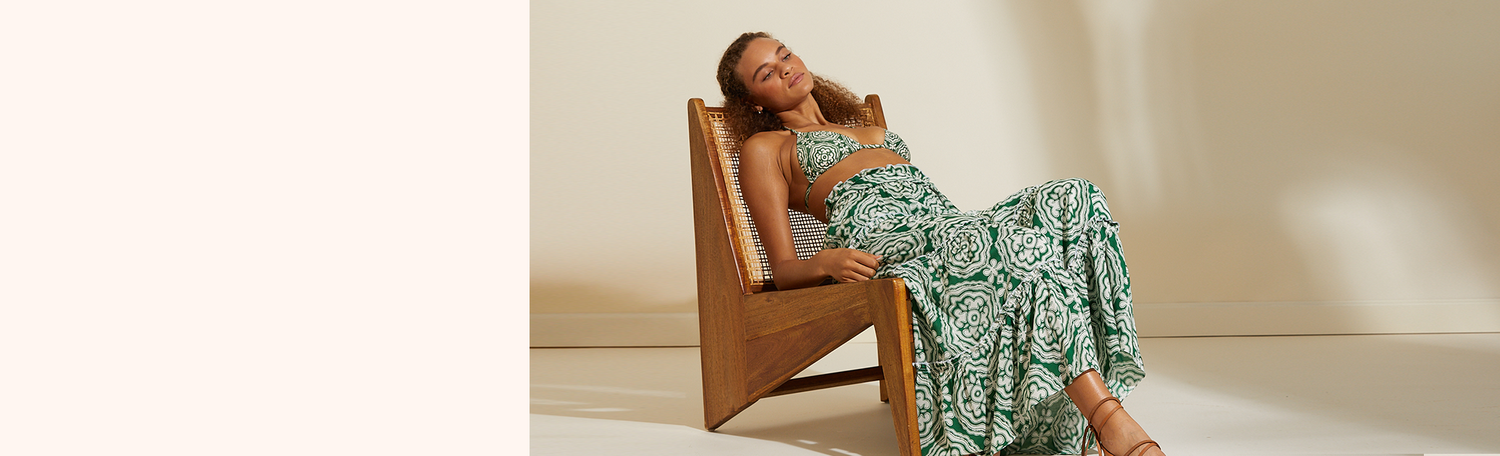 Woman lounging on a wooden chair wearing the Medallion Triangle Bikini Top and Matching Maxi Skirt. 