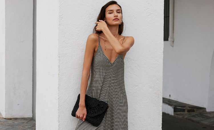 Woman standing in front of a white wall with her arms up by her head wearing a long silky brown and white slip dress. 