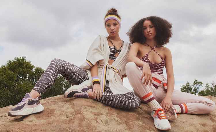 Woman do a plank on a rock with bush and rocky cliff in the background. She is wearing Puma x lemlem low impact bra and matching Puma x lemlem leggings in brown.
