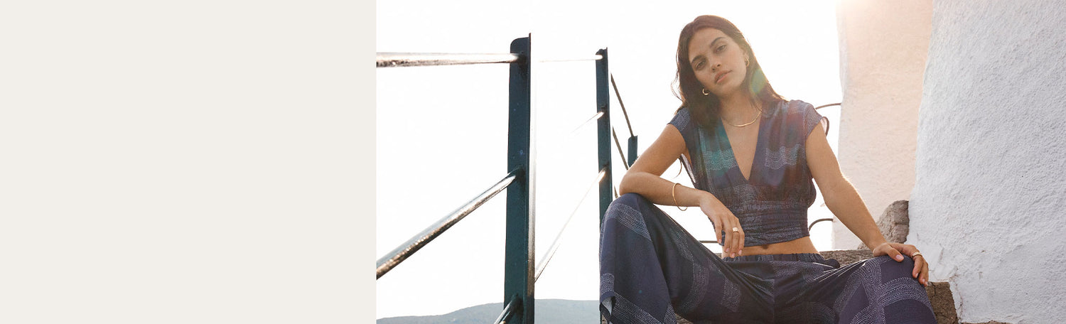 Woman sitting on stairs wearing a plunge crop top in silky navy blue and matching wide leg pants