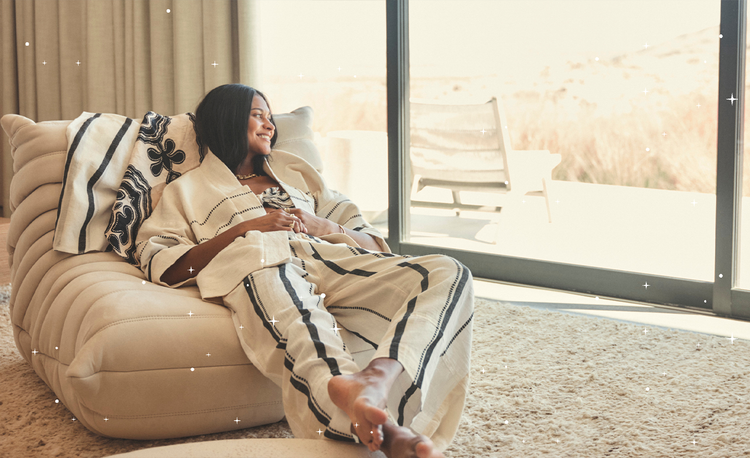 Woman sitting on a sofa in a bedroom wearing a handwoven matching set of cream, black and white pants and jacket