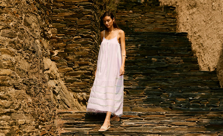 Woman walking on a rocky stairs pulling her hair around her head and wearing a light pink long slip dress.