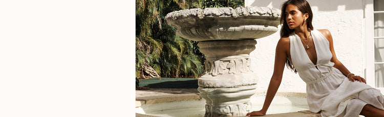 Woman sitting by a fountain wearing a long white lemlem dress.