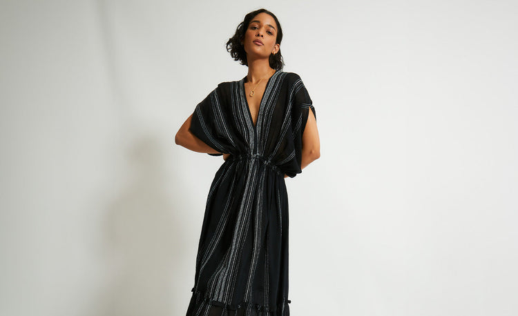 Woman Standing Wearing handwoven  lemlem Leliti Black Dress featuring stiched white pattern on black background 