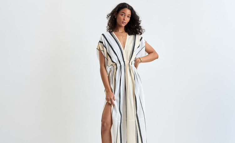 Woman standing wearing lemlem handwoven plunge dress featuring stripe pattern in black color on cream background
