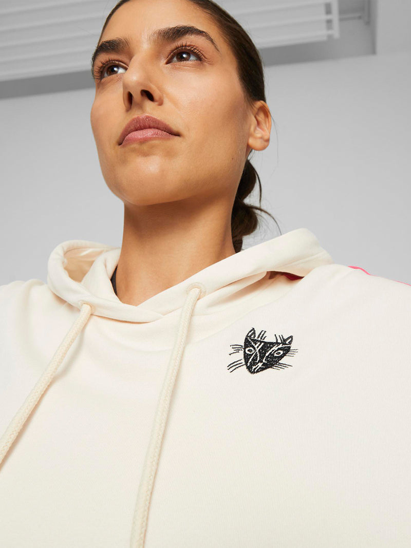 Close up on a woman standing wearing  Puma x lemlem oversized hoodie and joggers  in a Ghost Pepper Color featuring hand sketched cat logo and color block stripes in bright pink and yellow colors. 