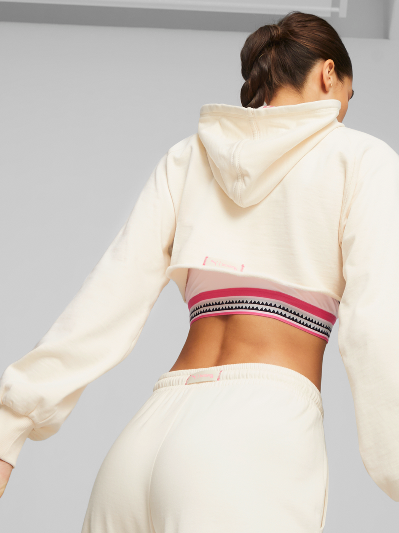 Back view of a Woman wearing Puma x lemlem Cropped Hoodie in Ghost Pepper Color featuring Handsketched puma logo, joggers in Ghost Pepper Color and Cropped Tank in Pink Color featuring lemlem signature Tibeb Print and color block details