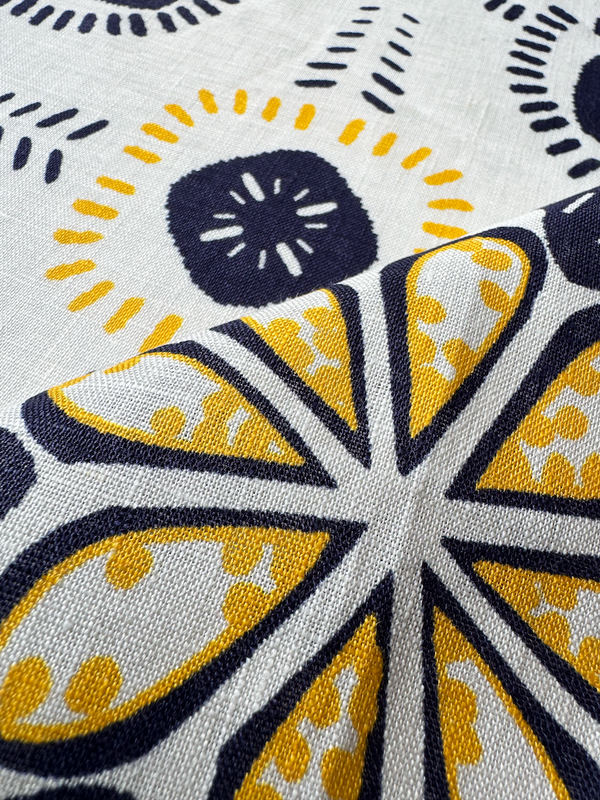 Close up on lemlem linen fabric featuring exclusive in-house–designed floral prints accented by ancient motifs, rendered in bright yellow and navy on an ivory background.