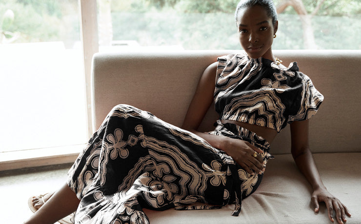 Woman sitting wearing lemlem linen MUNA Cropped Top and SANAA Maxi skirt featuring cream pattern on rich background