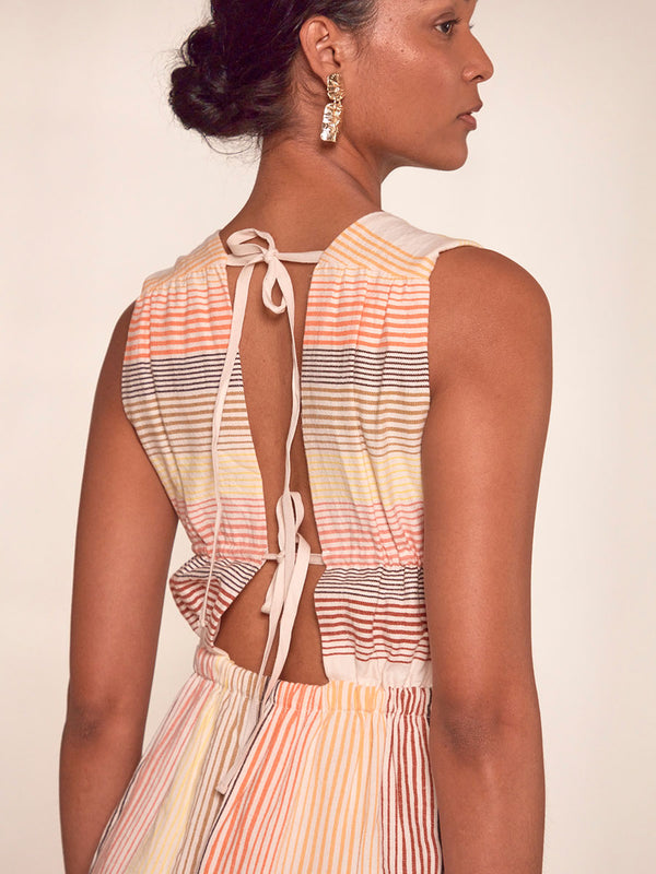 Close up on a back of a Woman Standing Wearing lemlem Anthea Dress featuring continuous stripe pattern in warm yellow, orange and peach tones