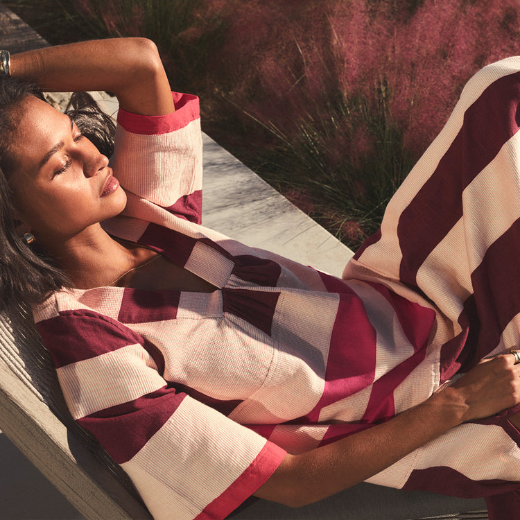 Woman wearing  red and white striped dress, lying on a stone surface with plants in the background