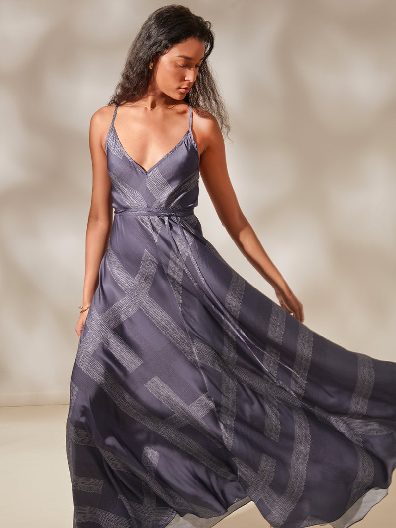 Woman Standing Wearing Aluna Slip Dress featuring an elegant hand-sketched chevron pattern, featuring alternating neutral and charcoal stripes set against a cool steel blue background.