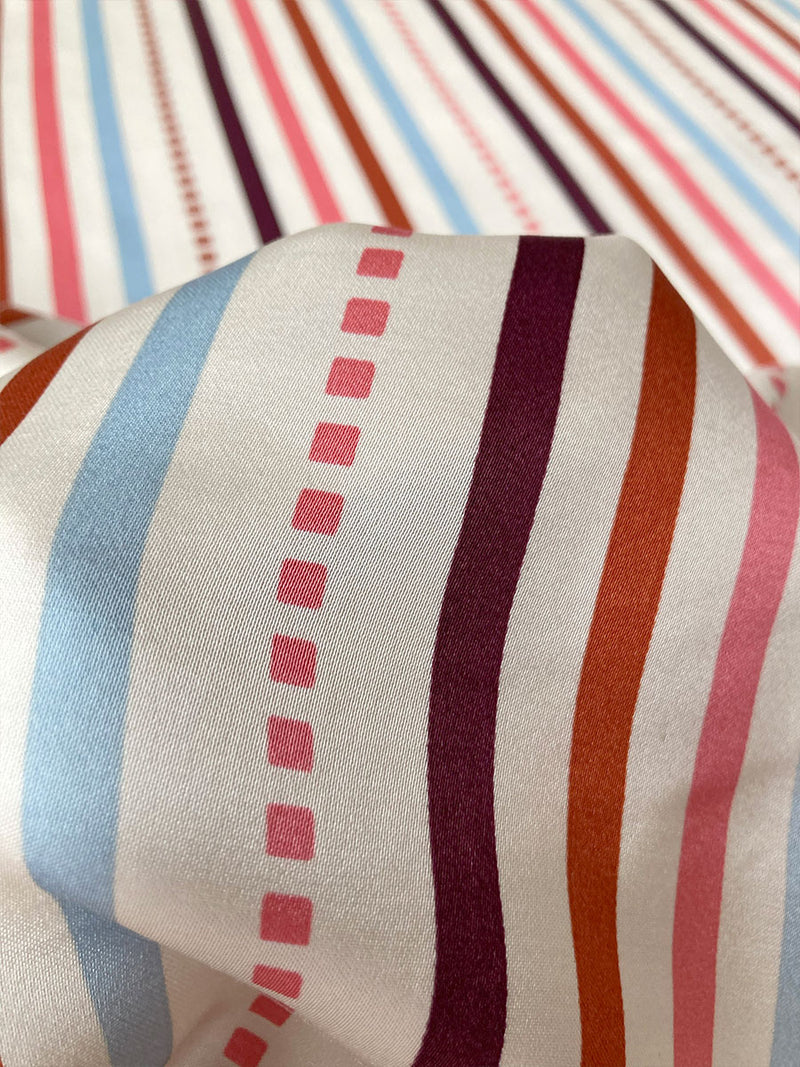 Close Up On Silky Bezu Cream Fabric featuring multi stripe pattern with geometric dots with Coral, Sky blue colors grounded by brown ground color on cream background.