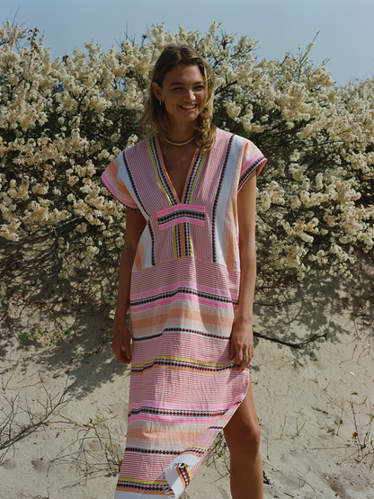 Woman standing on the Fire Island Beach Wearing Cirq Long Caftan Dress featuring pink, orange and yellow stripes and signature Tibeb design in burgundy bands.