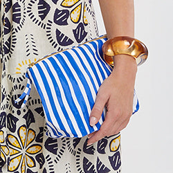 Close up on a woman standing holding the CORA Pouch featuring striped pattern in blue and white colors