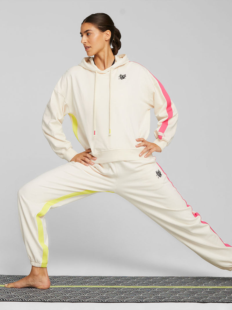 Woman Exercising on yoga mat wearing Puma x lemlem oversized hoodie and joggers in a Ghost Pepper Color featuring hand sketched cat logo and color block stripes in bright pink and yellow colors