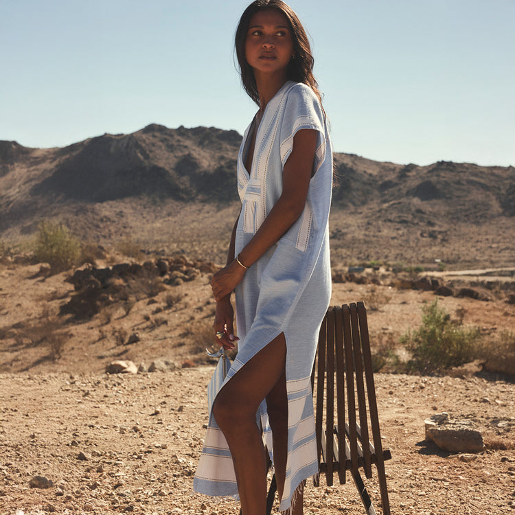 Woman in a light blue dress standing in a desert landscape with mountains in the background.