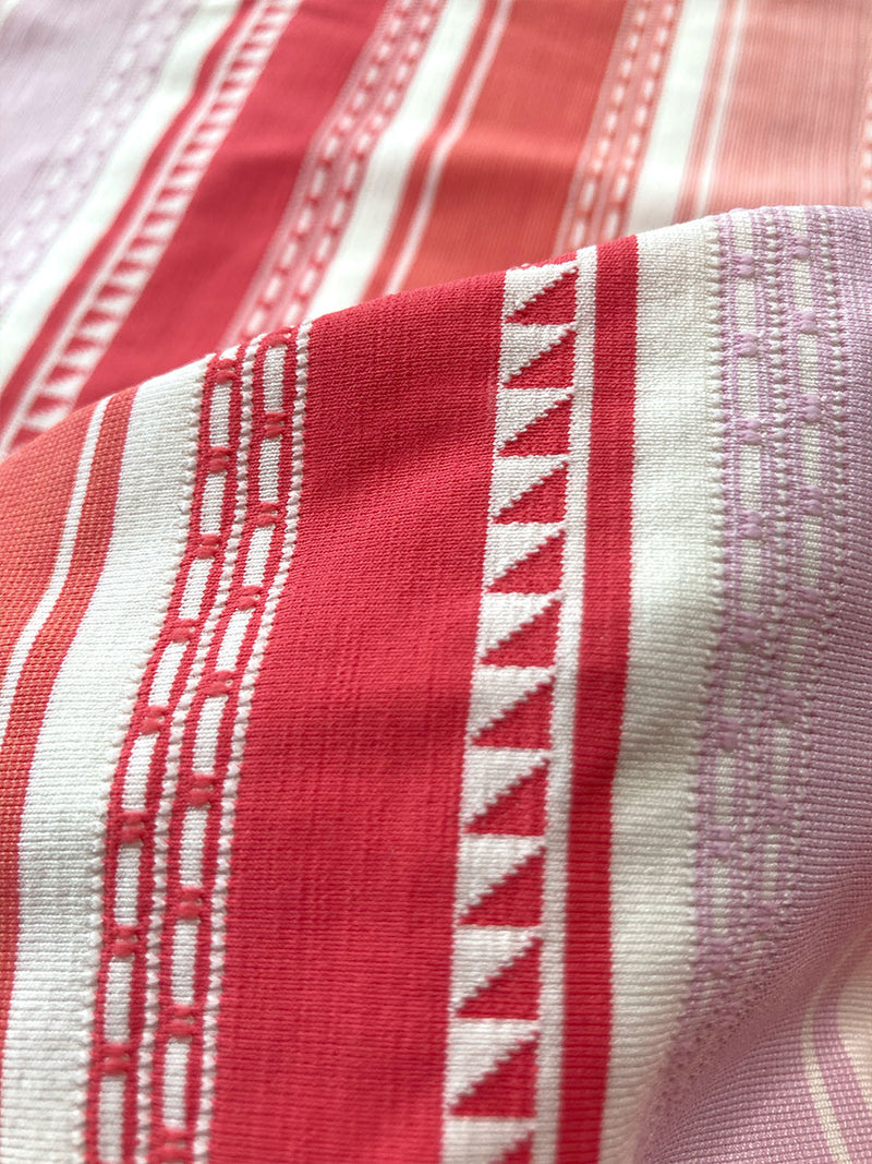 Close up on the fabric of the Eshal Triangle String Top featuring white doted stripes with gradiant orange and tangerine bands on a lilac and white background.