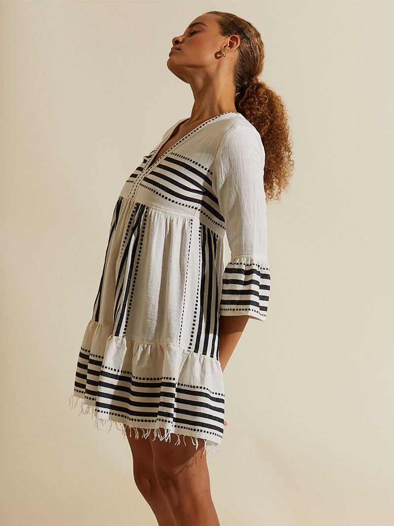 Woman standing wearing the Eshe Flutter Dress featuring architectural and textured black stripes and dotted lines on an off white background.