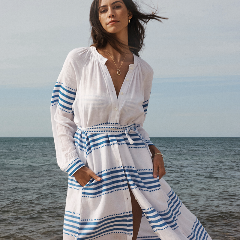 Woman standing on a beach with the ocean in the back wearing a long white and blue lemlem maxi dress.