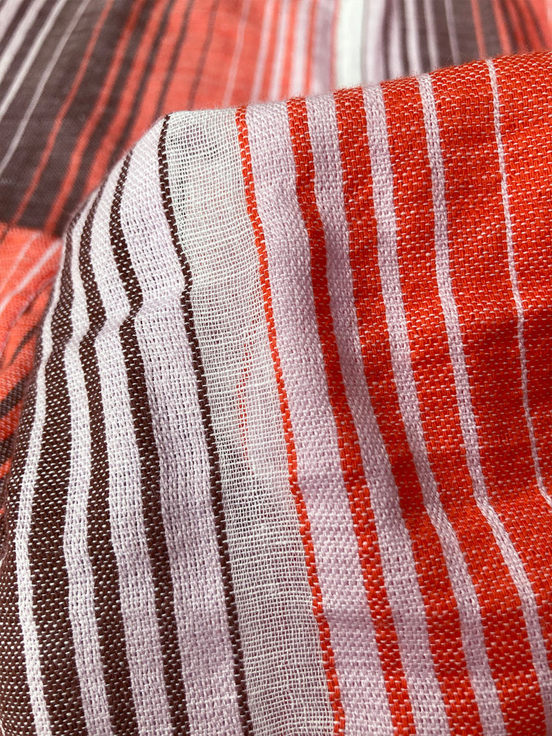 Close up on Feven Cayenne Fabric featuring graded continuous stripe pattern creating an ombre effect featuring earth, orchid & burnt orange.