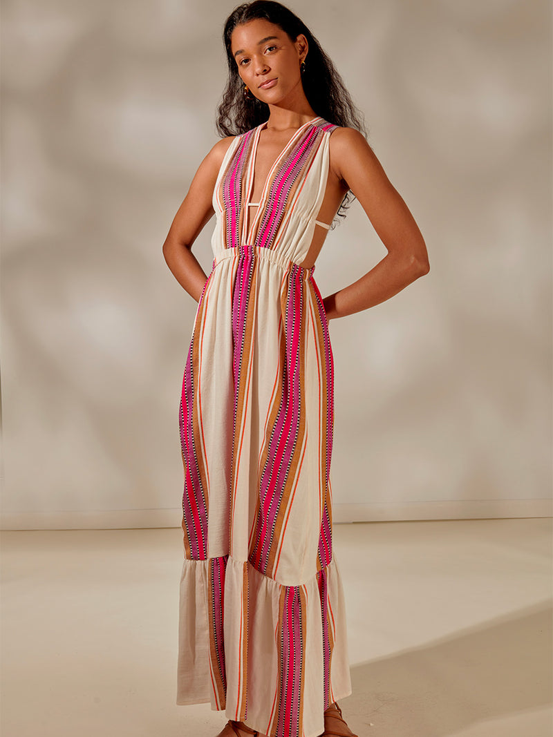 Woman Standing Wearing Lelisa V Neck Dress featuring stripe pattern in magenta, ochre, and berry tones, delineated by black and white dots and accented with a splash of neon orange on natural cotton background